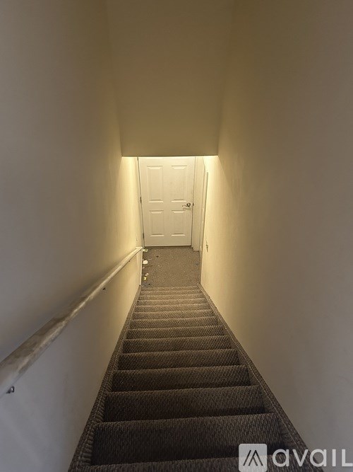 A long hallway with a carpeted staircase leading to a white door.