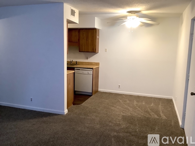 A carpeted room with a kitchen area and a door.