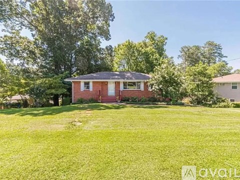 A red house with a white door and windows is surrounded by green grass and trees.