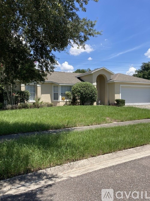 A house with a brown roof and a white garage door is surrounded by green grass and trees.