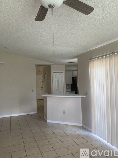 A room with a ceiling fan and a kitchen area in the background.