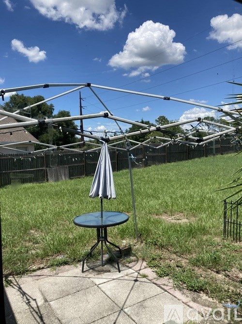 A table with a striped umbrella is in the foreground of a yard.