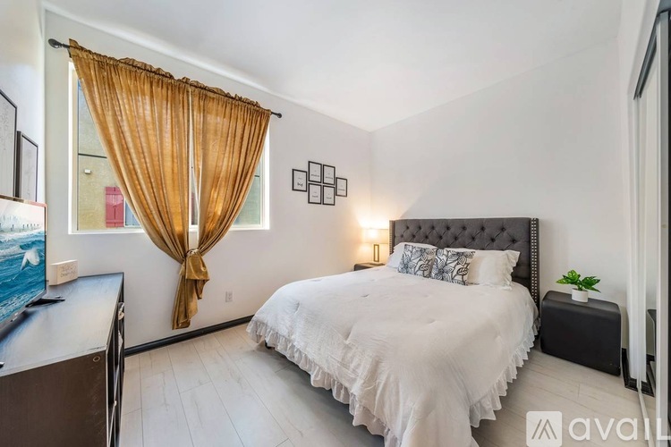 A bedroom with a bed, a television, and a window with curtains.