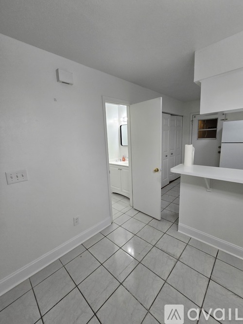 A white tiled kitchen with a refrigerator and a doorway leading to another room.