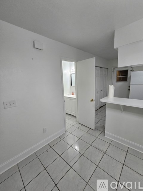 A white tiled kitchen with a refrigerator and a doorway leading to another room.