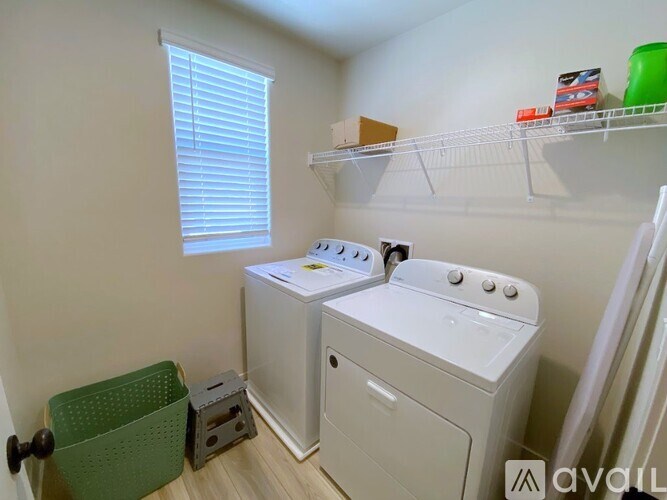 A laundry room with a washer and dryer, a green basket, and a shelf with a box and a red object on it.