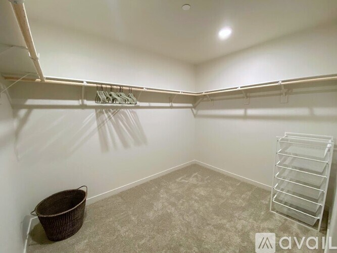 A room with a carpeted floor, a white wall, a white shelf, and a basket on the floor.