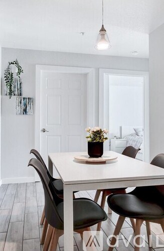 A white dining table with black chairs and a vase of flowers on top.