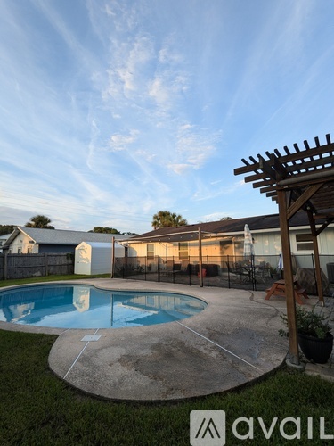A pool with a pergola and a house in the background.