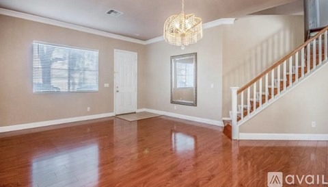 A spacious room with wooden floors and a staircase on the right side.