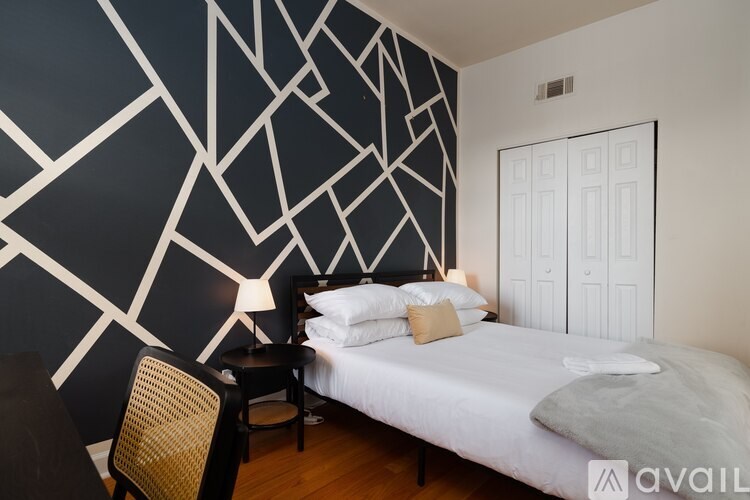 A bedroom with a white bed and a black and white geometric wallpaper.