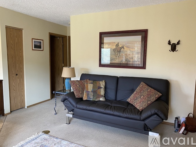 A living room with a black couch and a painting on the wall.