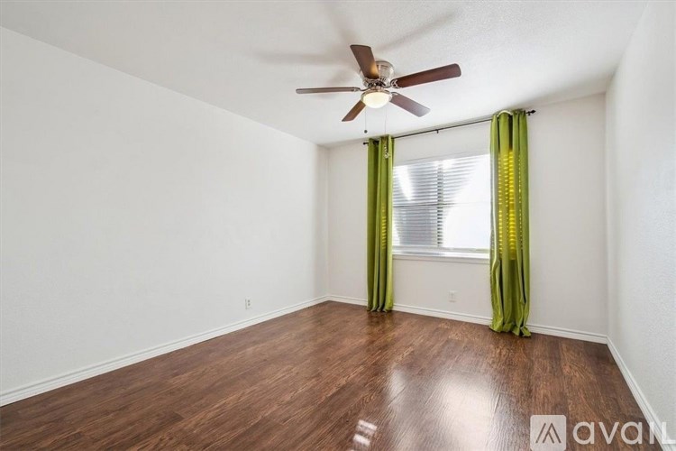 A room with a ceiling fan and a window with green curtains.