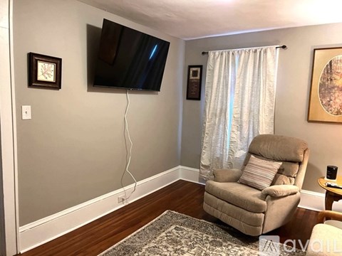 A living room with a beige chair and a flat screen TV mounted on the wall.