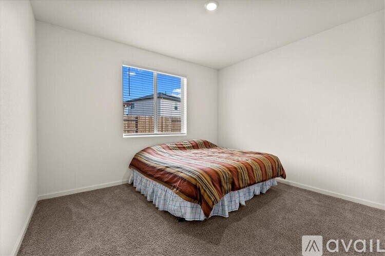 A bedroom with a bed and a window overlooking a fence.