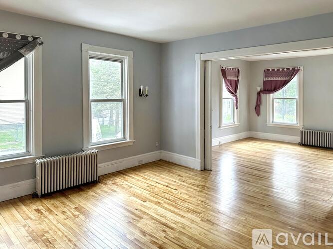 A room with wooden floors and two windows with curtains.