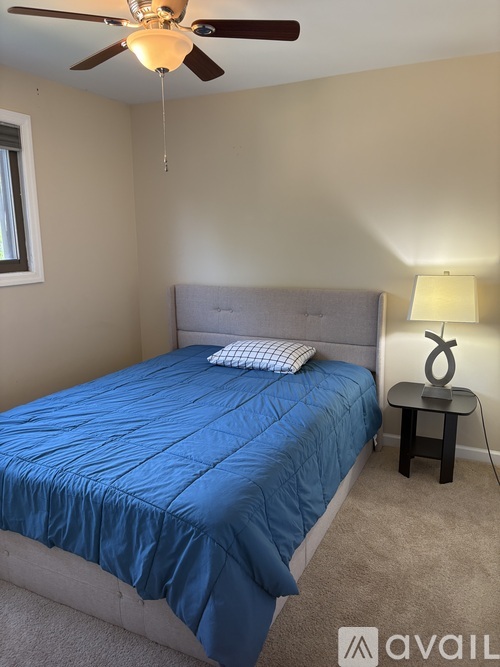 A bedroom with a blue bedspread and a ceiling fan.