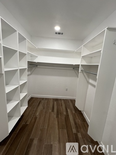 A spacious walk-in closet with white shelving and wooden flooring.