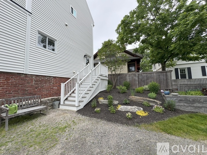 A house with a grey siding exterior and a small garden area with a bench and a gravel path.