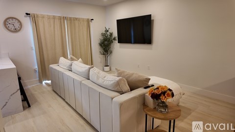 A living room with a white couch, a small table with a vase of flowers, and a flat-screen TV mounted on the wall.