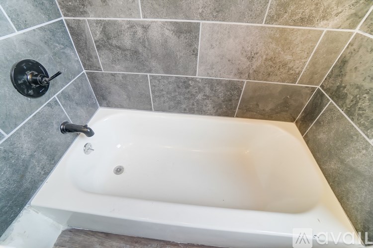 A white bathtub is in a bathroom with grey tiled walls.