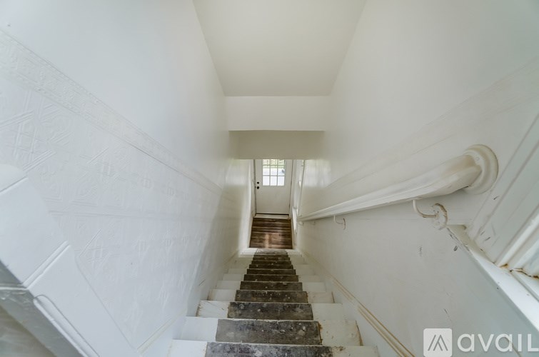 A staircase with a white wall on the side and a window in the distance.