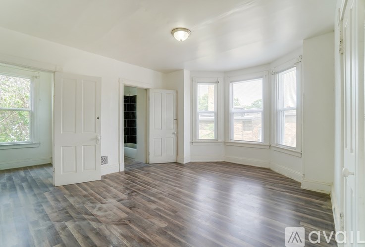 A room with wooden floors and white walls, with a window on the left side.