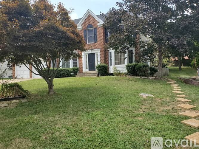 A brick house with a white door and windows is surrounded by a green lawn and trees.