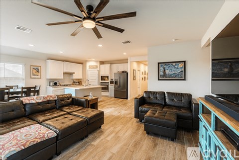 A living room with a black leather couch and a ceiling fan.