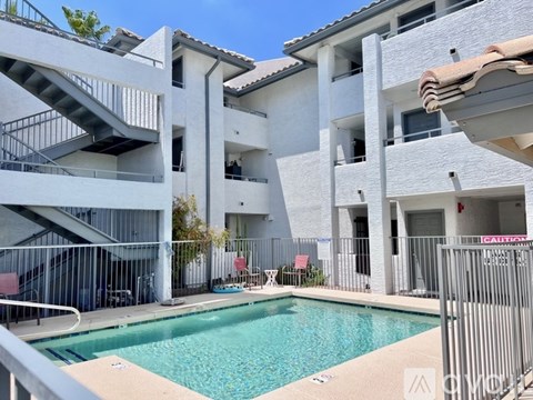 A swimming pool is surrounded by a white building with a metal fence.