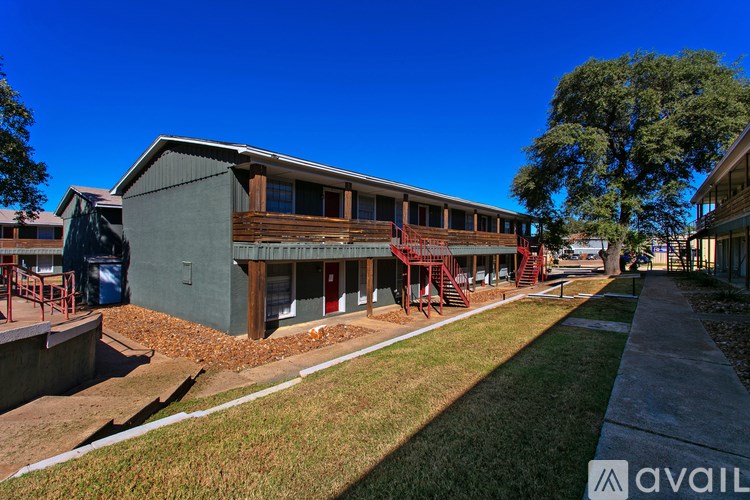 A building with a green exterior and a red door is surrounded by a grassy area and a concrete walkway.
