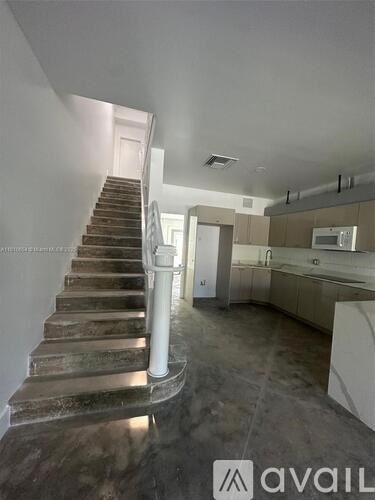 A staircase with a white railing leads up to a doorway in a room with a kitchen area.