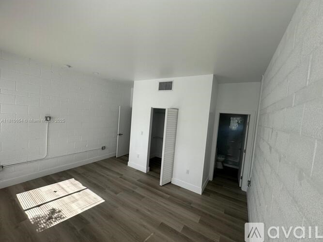 A room with white walls and wooden flooring, with a doorway leading to another room.