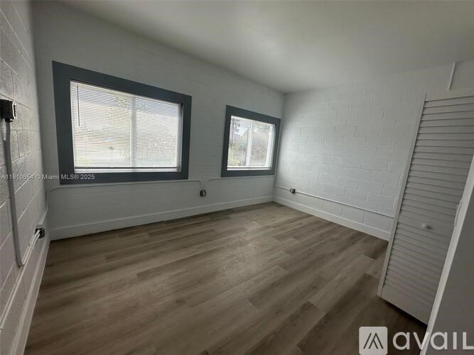 A room with wooden flooring and two windows.