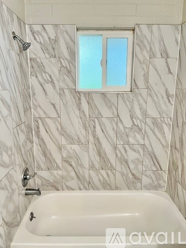 A bathroom with a marble tile wall and a white bathtub.