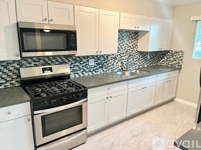 A kitchen with white cabinets and a black and white checkered backsplash.