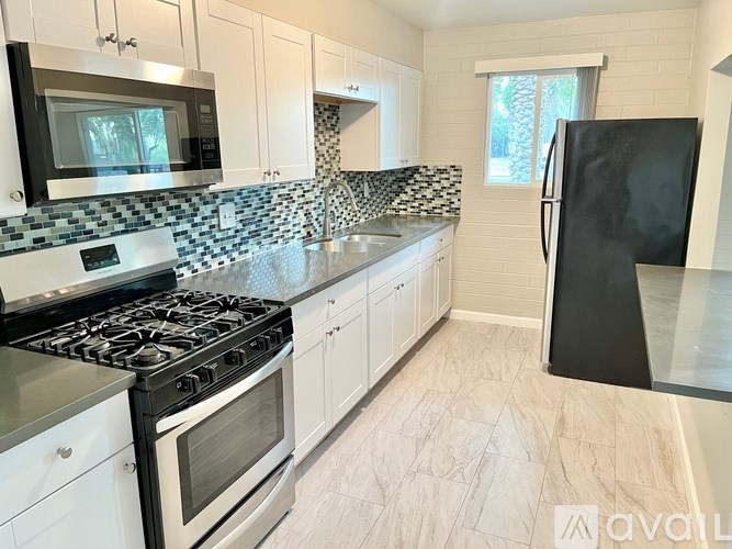 A kitchen with a black fridge, white cabinets, and a black and white tiled backsplash.