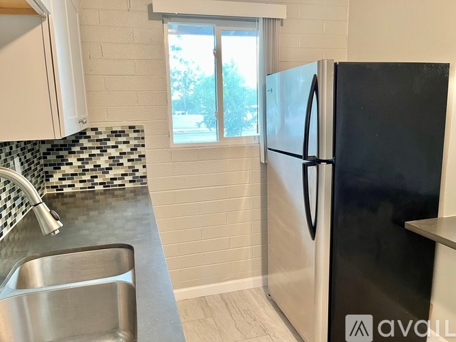 A black fridge stands next to a sink in a kitchen.