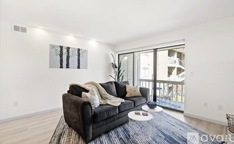 A living room with a black couch and a painting of trees on the wall.
