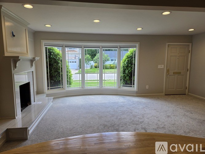 A spacious living room with a fireplace and large windows overlooking a green lawn.