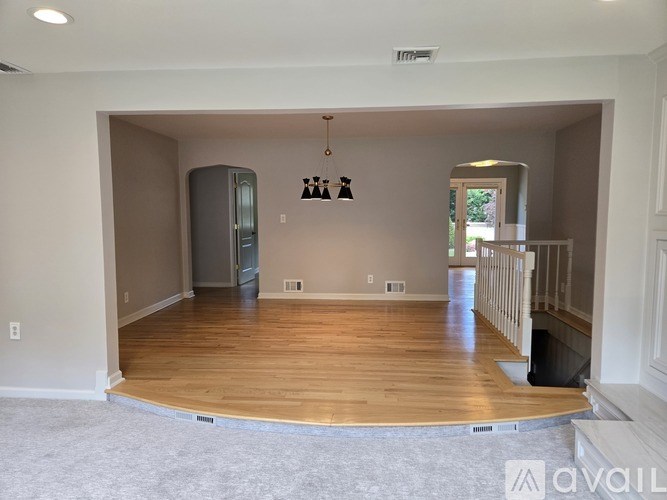 A large empty room with wooden flooring and a staircase on the right side.