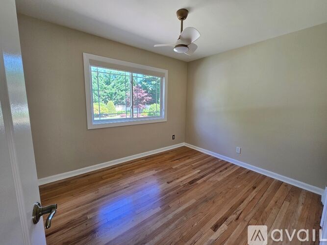 A room with wooden flooring and a window showing trees outside.
