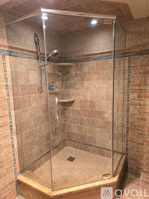 A shower with a glass door and a brown tiled wall.