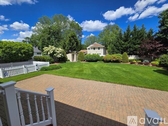 A backyard with a white fence and a brick patio.