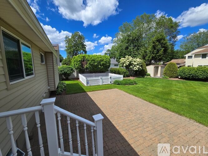 A sunny day in a residential area with a house, a white picket fence, and a well-kept lawn.