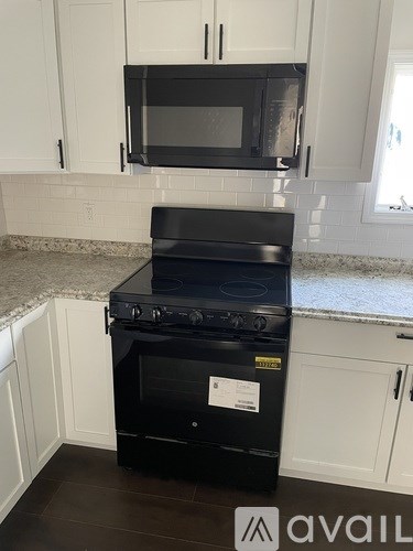 A black stove and microwave in a kitchen with white cabinets.