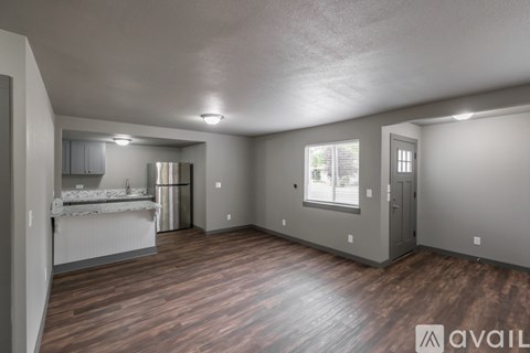 A spacious room with wooden floors and a kitchen area with a sink and refrigerator.