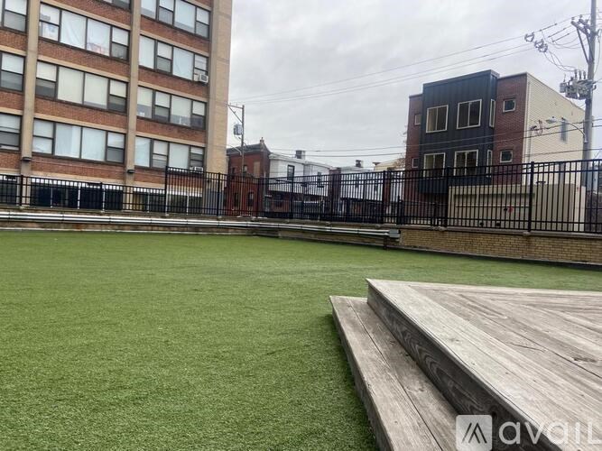 A green artificial turf soccer field with a wooden platform in front of a brick building.
