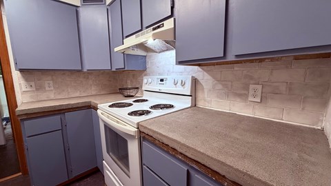 A kitchen with a white stove top oven and blue cabinets.