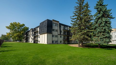 A large grassy area in front of a building with trees.